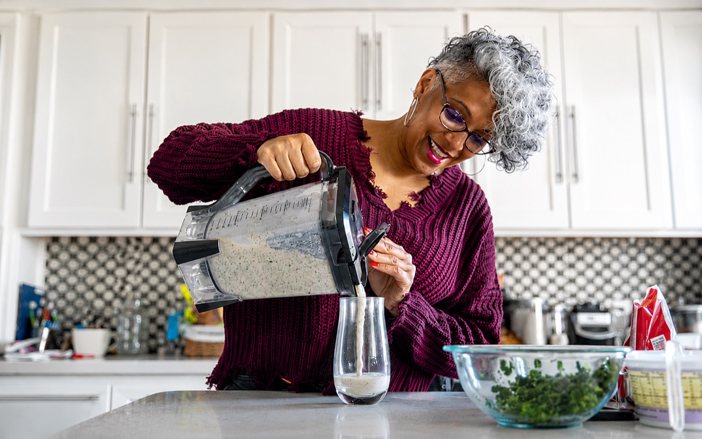 Woman pouring a homemade smoothie in a bright kitchen